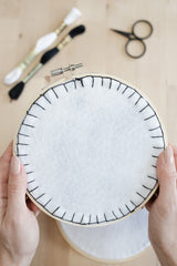 A finished embroidery hoop with a white felt backing and black blanket stitch thread