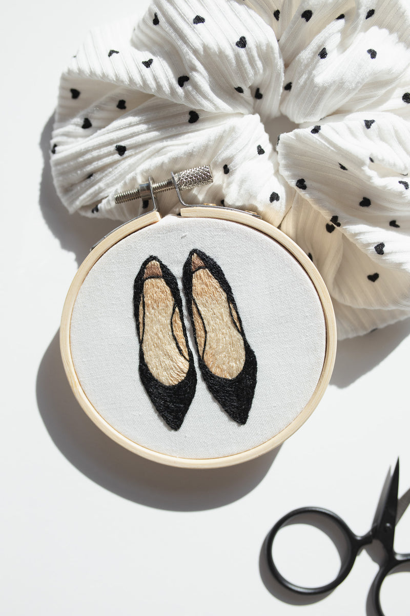 Finished mini embroidery project featuring black high heels leaning against white scrunchie with black scissors
